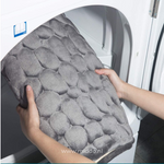 Handen plaatsen een grijze kiezelsteen-achtige badmat in de wasmachine voor reiniging