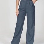 Een vrouw die staat met witte slippers  aan en heeft de wijdepantalon in blauw aan.