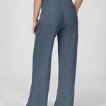Een vrouw heeft de wijde blauwe pantalon aan maar laat nu de pantalon zien met 2 zakken op de achterkant van de broek.